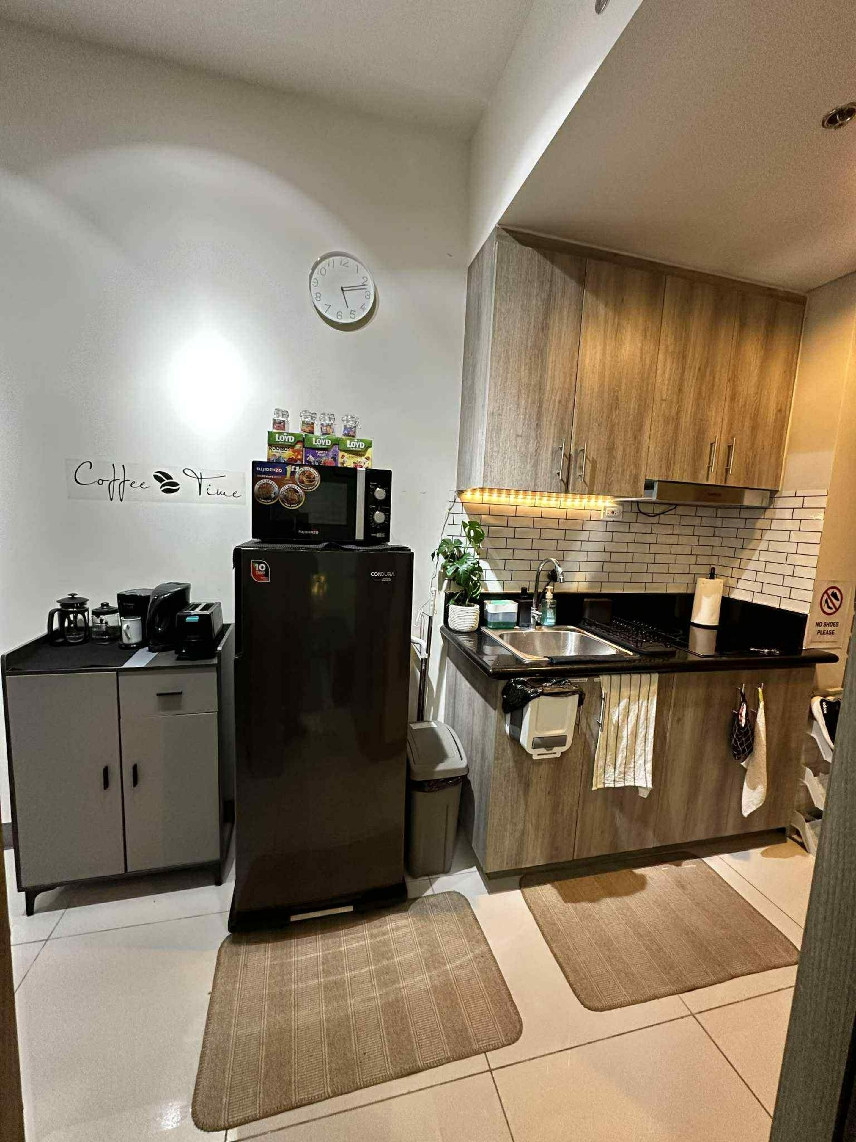 A compact kitchen with a refrigerator, microwave, and a clock on the wall.
