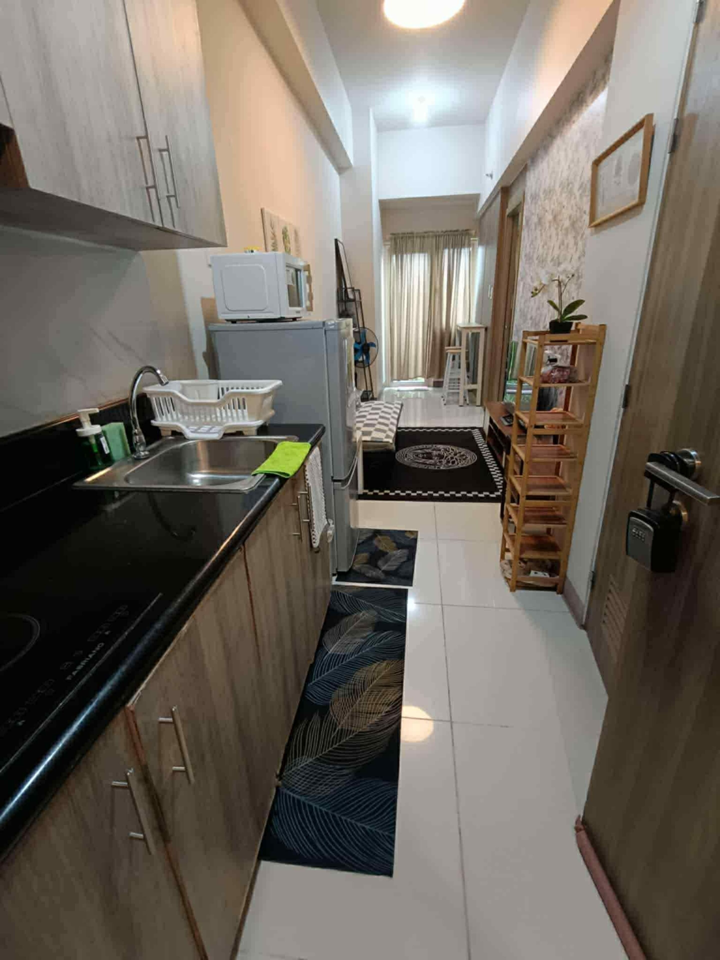 A compact kitchen with a black countertop, a sink, and a microwave. There is a small dining area with a table and chairs, and a bookshelf with a plant.