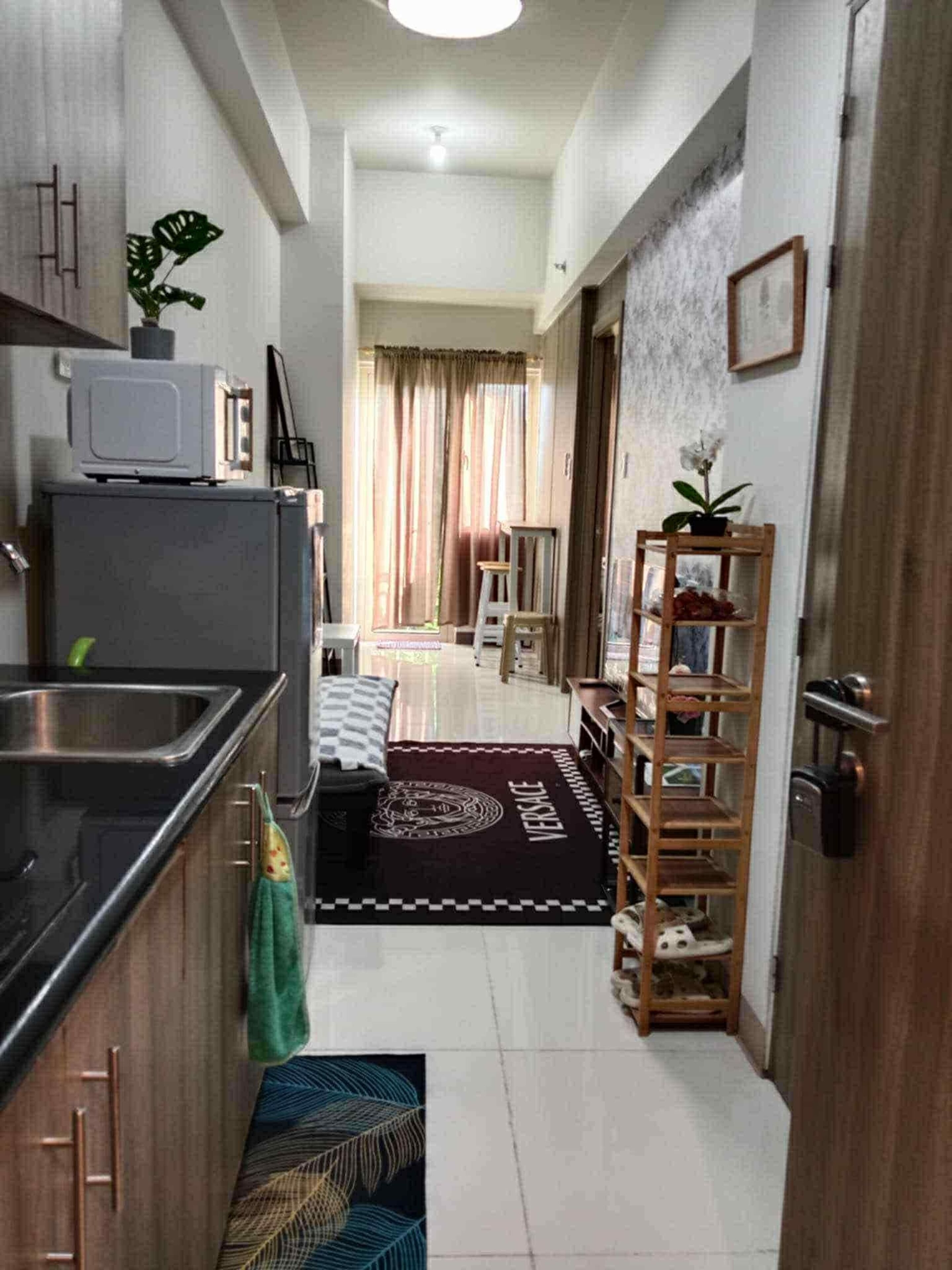 A narrow hallway with a kitchen area on the left, a wooden door on the right, and a living area in the background.