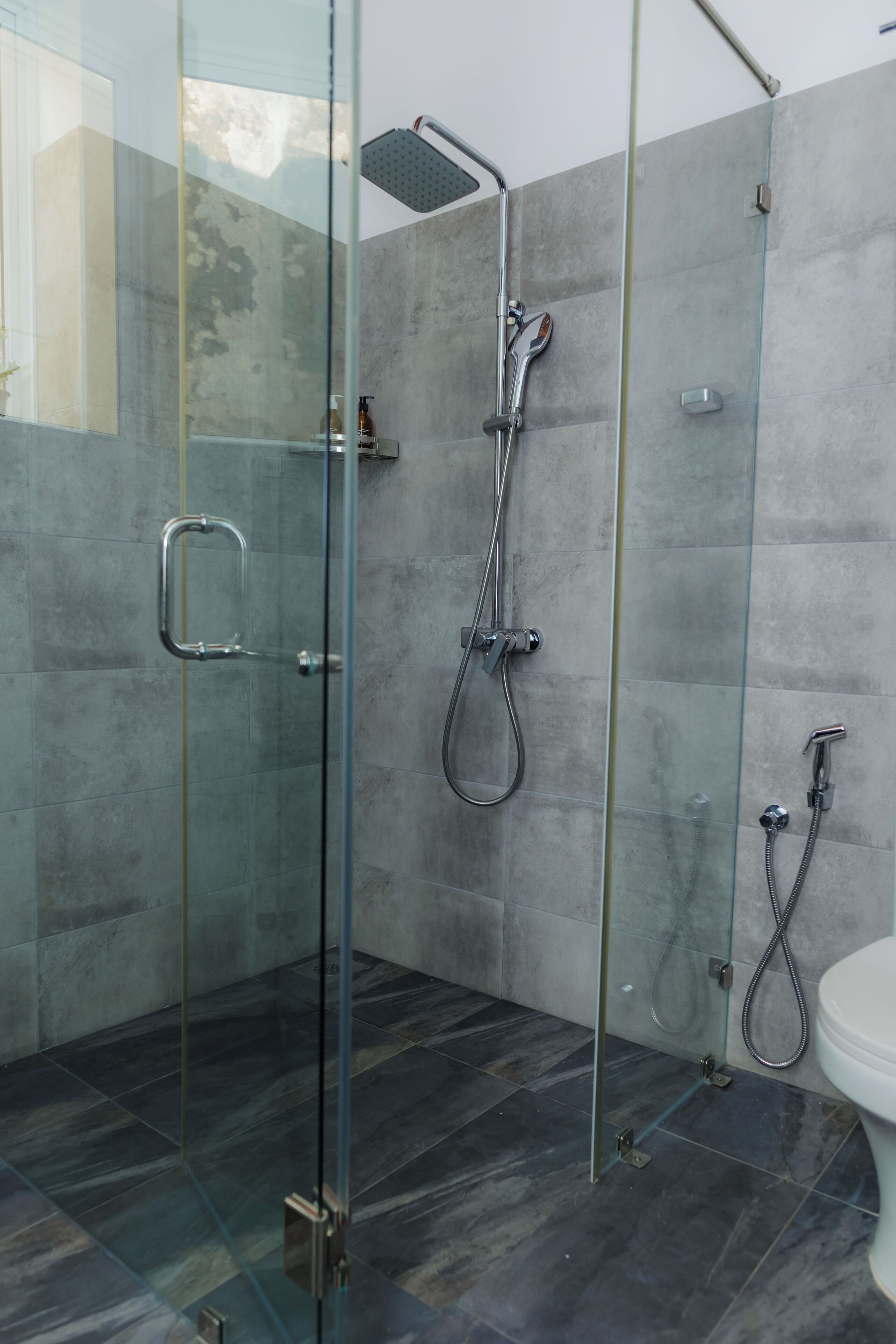 Ein modernes Badezimmer mit einer Duschkabine aus Glas, einer Handbrause und einem am Wand montierten Wasserhahn.