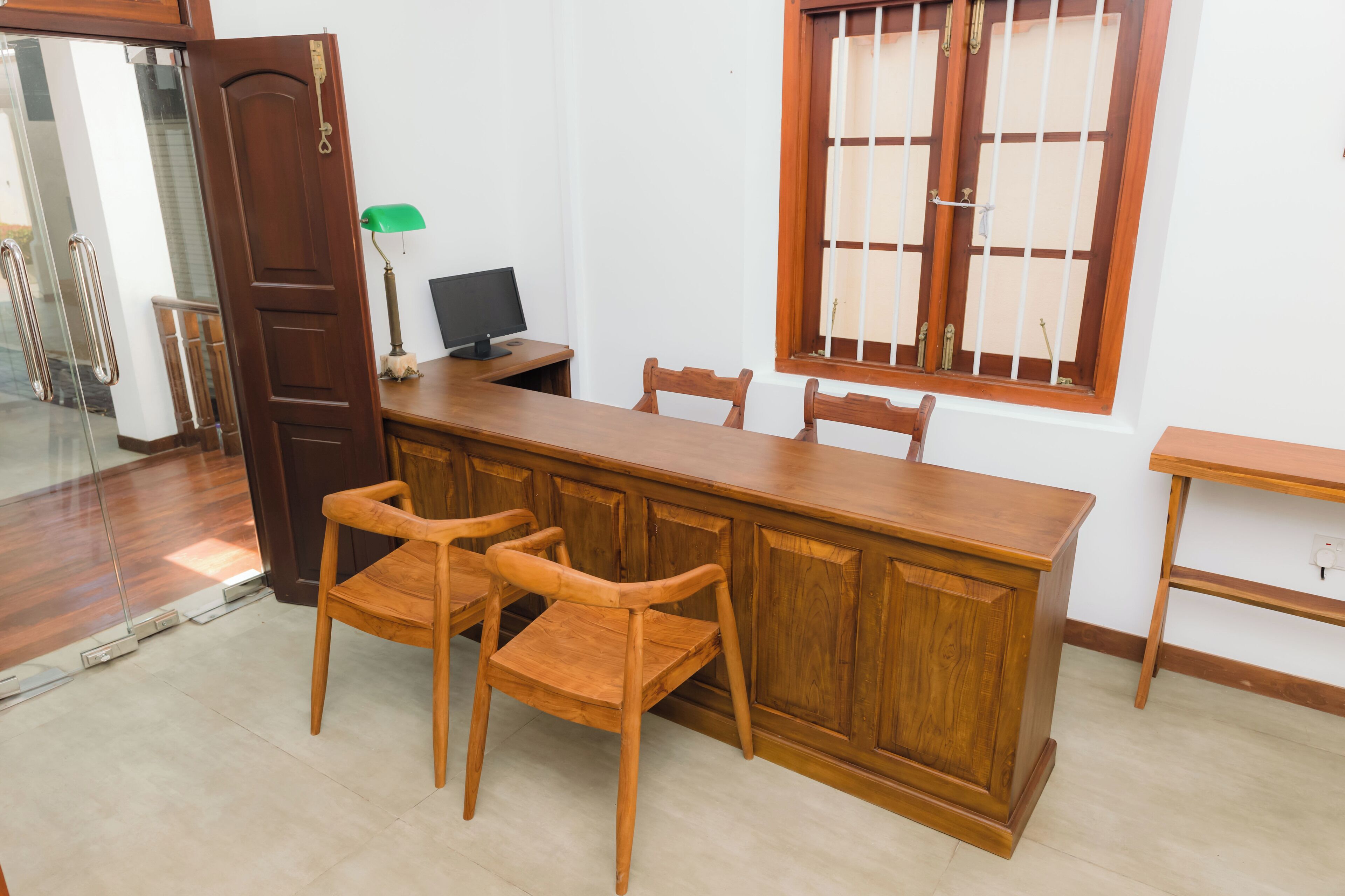 Une table à manger en bois avec quatre chaises, un ordinateur sur un bureau et une fenêtre avec des barreaux.