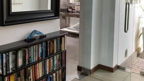 Una sala de estar moderna con una estantería, un espejo grande y una puerta de cristal que da a una cocina.