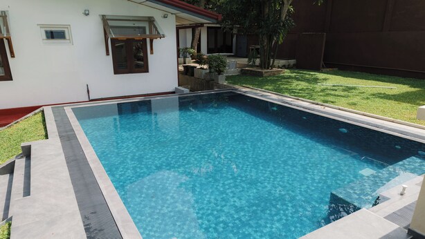 Una piscina rectangular con agua azul cristalina, rodeada por una solana de hormigón y una pequeña zona verde.