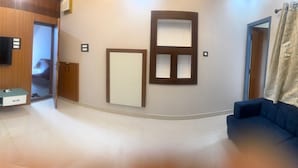 A modern living room with a flat-screen TV, a built-in bench, a large mirror, and a blue sofa. - MSK Homestay Service Apartment (Hubli)