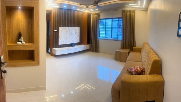 A modern living room with a wooden cabinet, a TV mounted on the wall, a sofa, and a window with curtains. - MSK Homestay Service Apartment (Hubli)