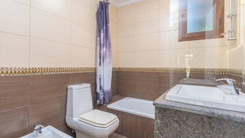 A bathroom with a toilet, bidet, bathtub, and a sink.