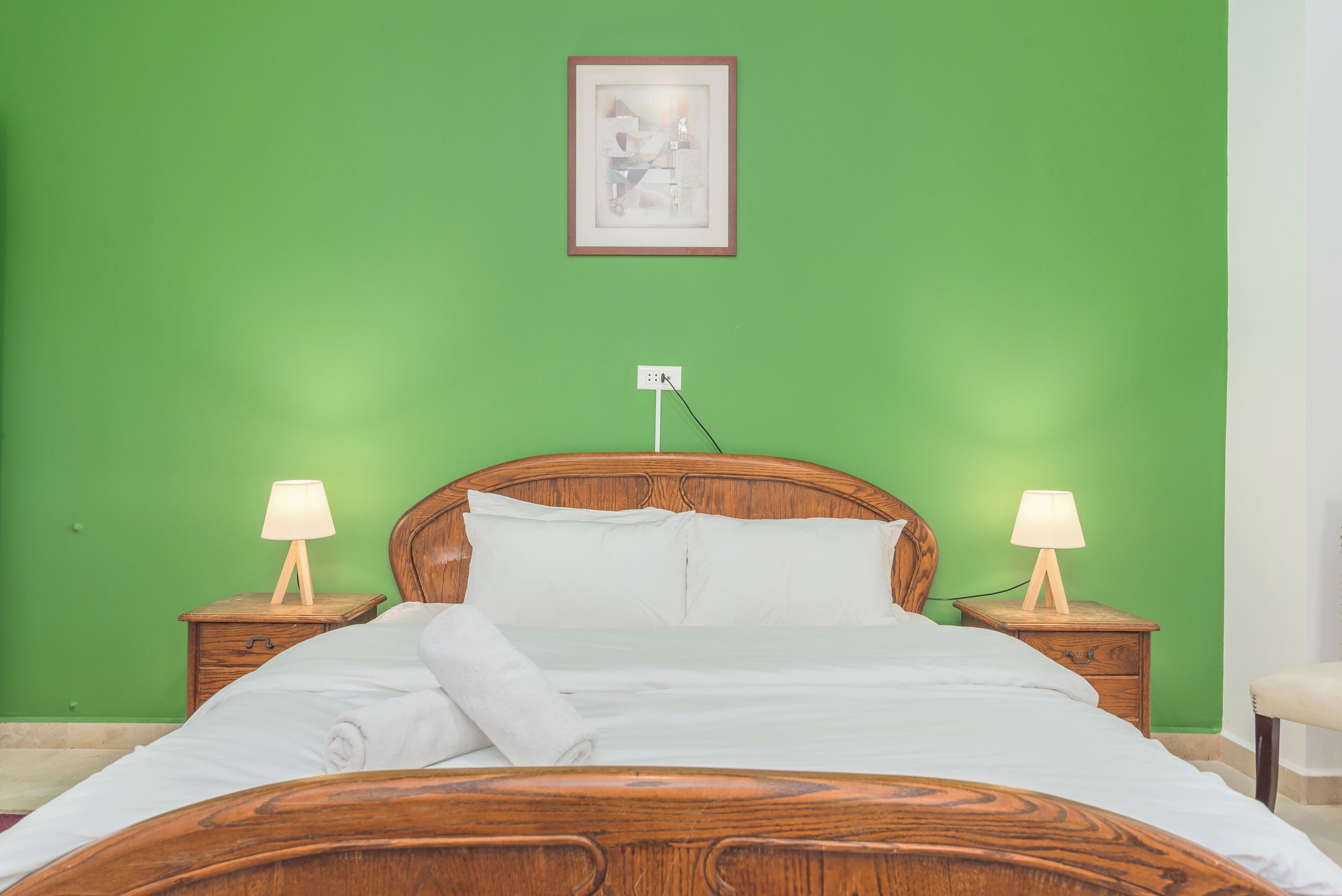 Un letto rifatto con lenzuola bianche, due comodini con lampade e una parete verde.