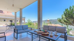A spacious outdoor seating area with a table set for dining, overlooking a scenic landscape with hills and a dome structure. - Beit Salima 3BR House with Pool (Salima)