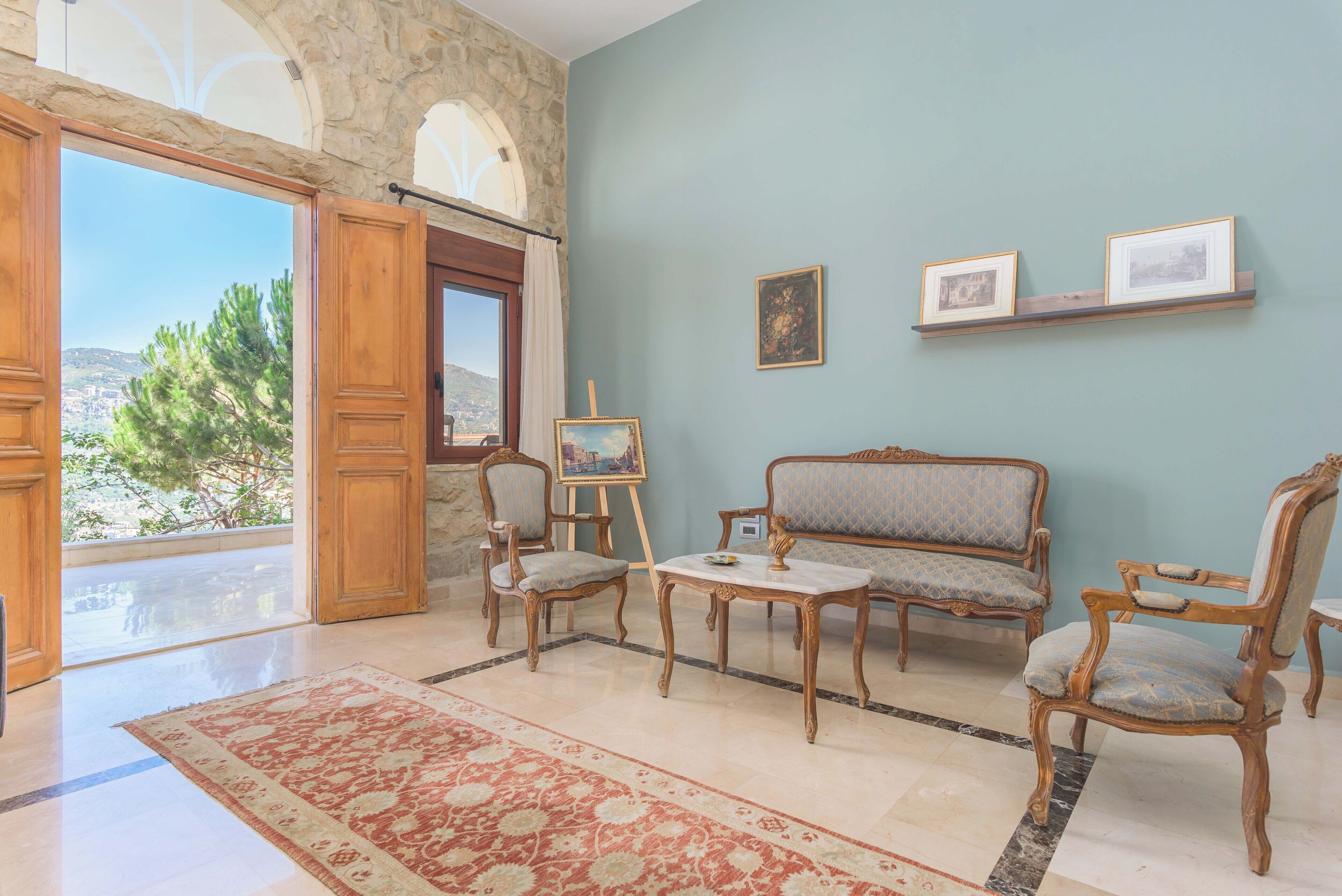 A room with a stone archway, a wooden sofa, two chairs, a small table, and a red patterned rug.