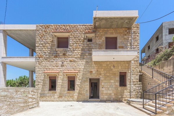 A stone building with a flat roof, a central door, and two windows on the ground floor.