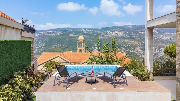 A terrace with a table and chairs overlooking a mountainous landscape, a pool, and a view of a church tower. - Beit Salima 3BR House with Pool (Salima)