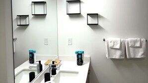 Une salle de bain moderne avec un grand miroir, un lavabo blanc et deux porte-serviettes.