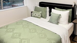 Une chambre à coucher avec un lit, une fenêtre avec des stores, une table de chevet et une commode.