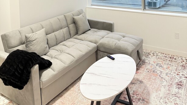 Un salon moderne avec un canapé, une table basse et une grande fenêtre équipée de stores.