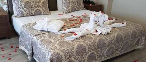 Una habitación de hotel con una cama grande, dos mesitas de noche y una mesita con lámpara.