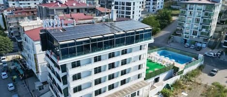 Un edificio moderno con un panel solar en la azotea, una piscina y una estructura de varios pisos con balcones.