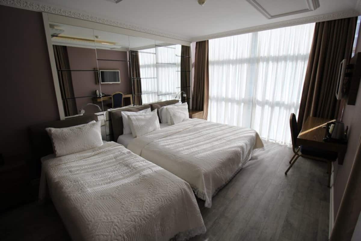 Hotelkamer met twee bedden, een bureau, een stoel, een televisie en een groot raam met gordijnen.
