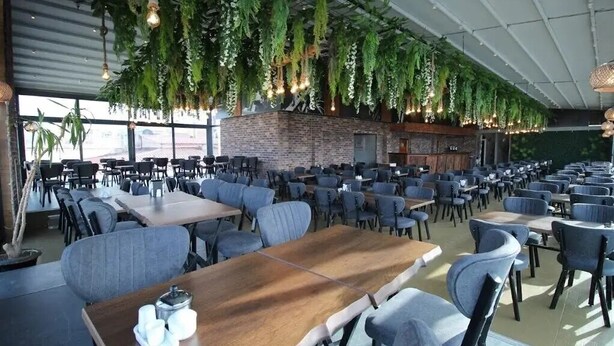 A spacious indoor dining area with multiple tables and chairs, a brick wall, and hanging greenery. - Atakum Palas Otel (Atakum)