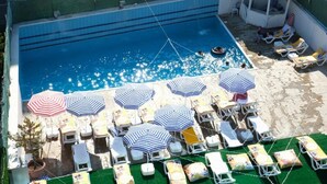 An outdoor swimming pool with multiple lounge chairs and umbrellas, surrounded by a barbed wire fence. - Atakum Palas Otel (Atakum)