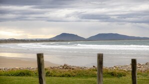 Una playa con olas, una valla y montañas al fondo.