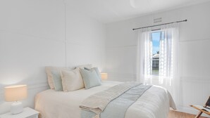 Un dormitorio con cama, mesita de noche, lámpara y ventana con cortinas.