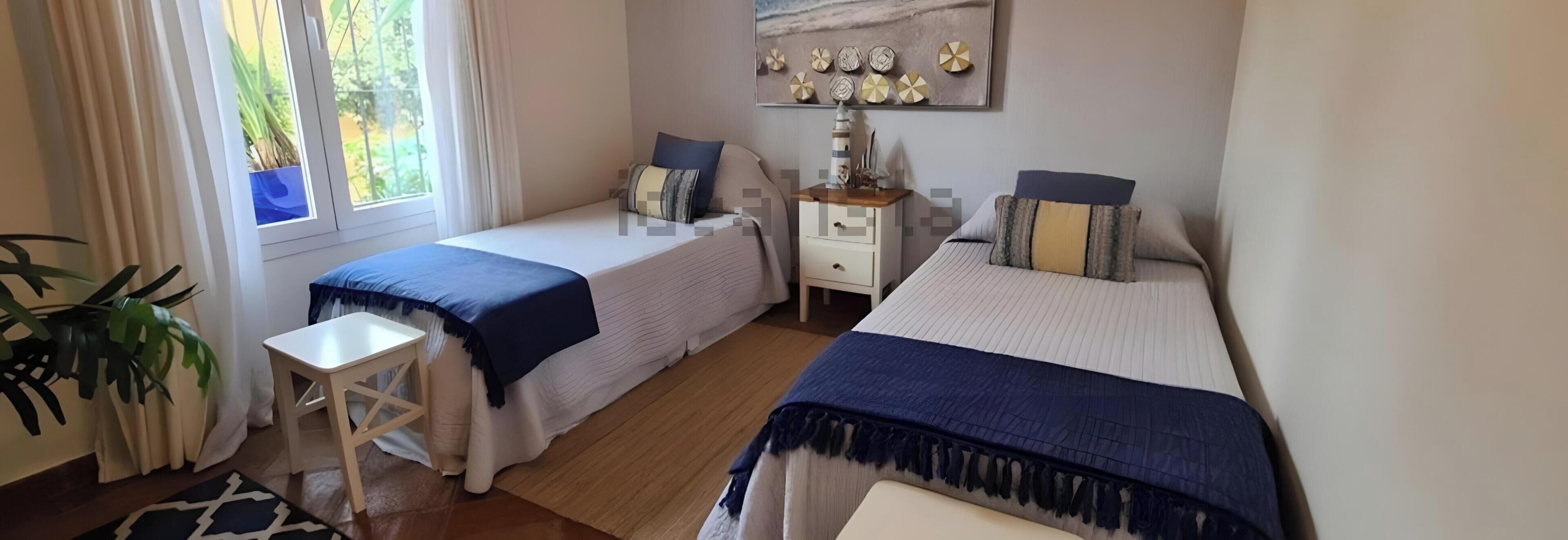Une chambre avec deux lits, une table de chevet, une lampe et une fenêtre avec des rideaux.
