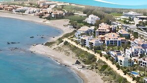 Una zona residencial costera con propiedades frente al mar, una playa de arena y un terreno montañoso.