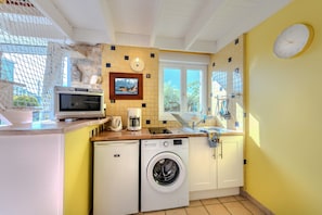 A compact kitchen with a washing machine, microwave, and a small window.