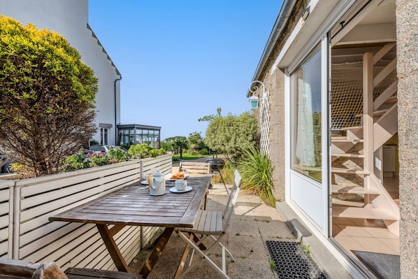 A patio with a wooden table and chairs, a white fence, and a building with a glass door.