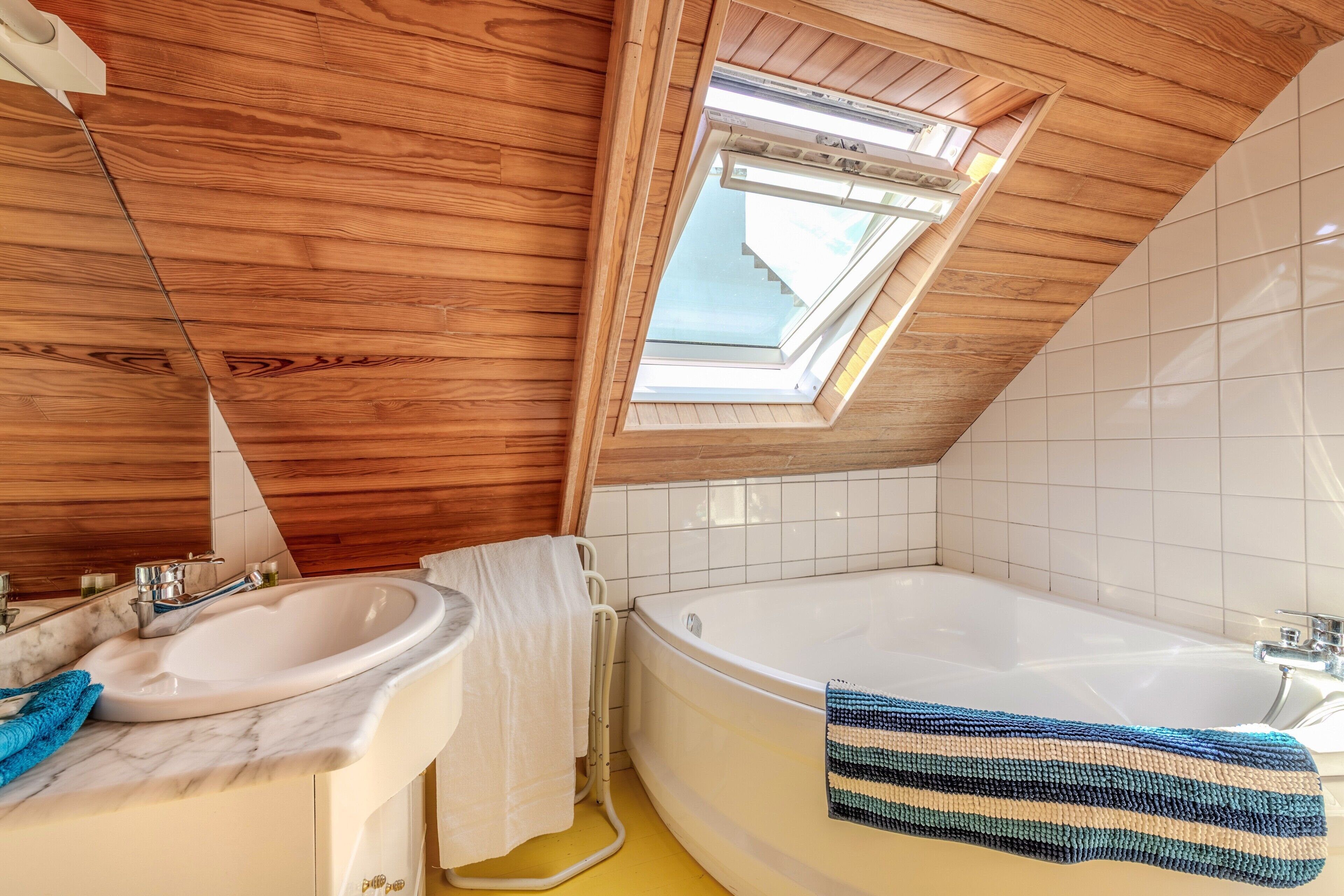 Un baño con techo de madera, tragaluz, bañera, lavamanos y toallero.