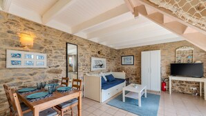Ein Zimmer mit Steinwänden, einem Esstisch, einer Couch und einem Fernseher.