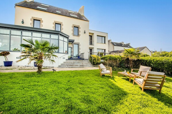 A modern house with a large glass bay window, a well-maintained lawn, and outdoor furniture.