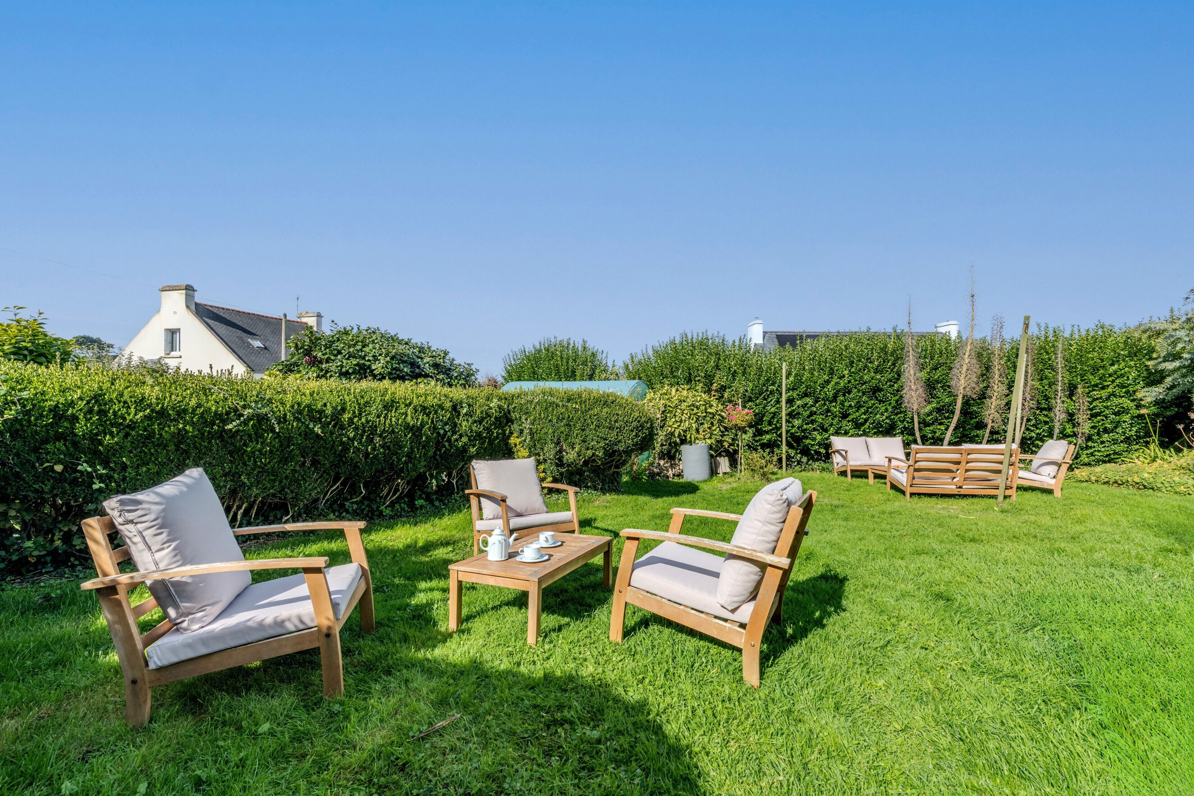 A garden with wooden furniture, including chairs and a table, and a hedge in the background.