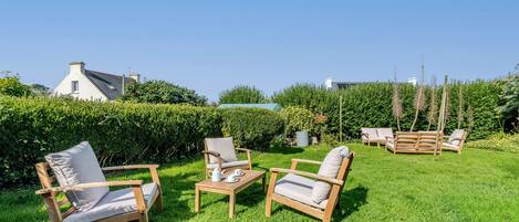 A garden with wooden furniture, including chairs and a table, and a hedge in the background.