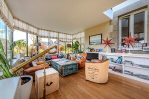 A spacious living room with a large window, leather furniture, a bookshelf, and decorative star-shaped objects.