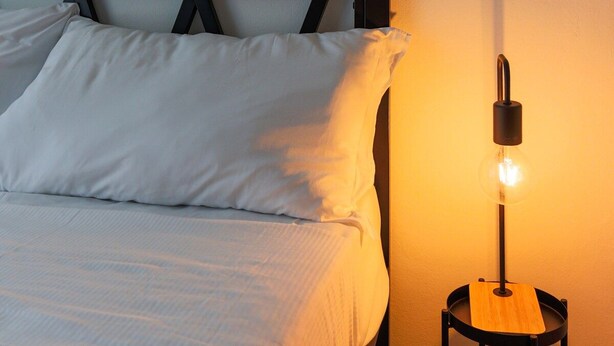 Une chambre à coucher avec un lit, des oreillers, une table de chevet avec une lampe et deux œuvres d’art florales accrochées au mur.