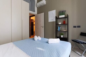A hotel room with a bed, a chair, a bookshelf, and a door leading to another room.