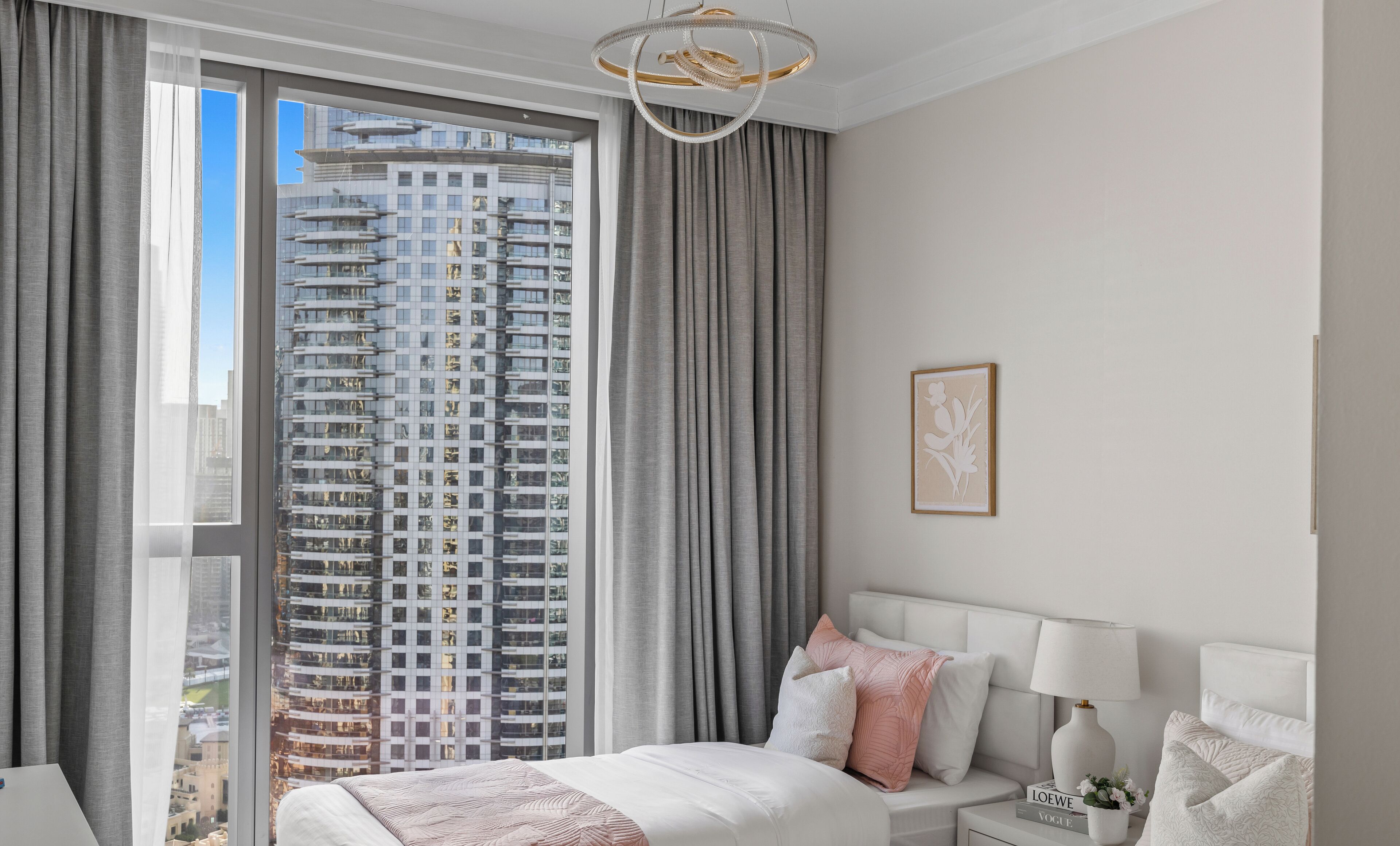 Una habitación de hotel moderna con un ventanal grande, una cama con cabecero blanco y una mesita de noche con lámpara.