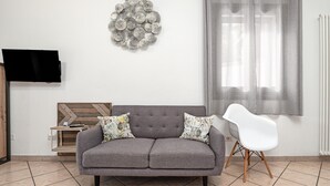A living room with a grey sofa, a white chair, a wall-mounted TV, and a decorative wall piece. - Apartment 'Sarda Bella Private Pool' with Mountain View, Wi-Fi and Air Conditioning (Rudalza)