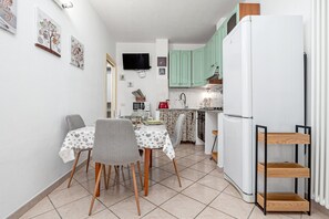 Eine kleine Küche mit Esstisch, Stühlen, einem Kühlschrank und einem an der Wand befestigten Fernseher.