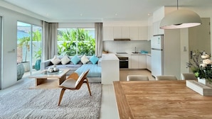 Een moderne keuken met witte kastjes, een houten eettafel en een groot raam met uitzicht op een tuin.