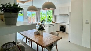 Een moderne keuken met een houten eettafel, hanglampen en uitzicht op groen buiten.