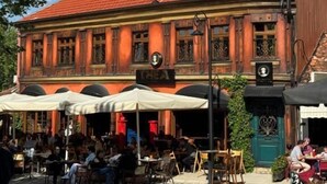 An outdoor café with tables and chairs, a building with a red-tiled roof, and a tall tower in the background. - Thea Hotel  (Prizren)