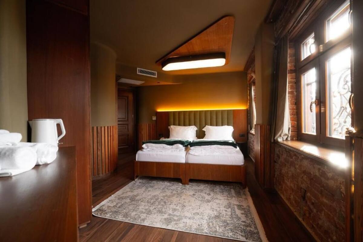 A hotel room with a wooden bed, a bedside table with a white pitcher, and a large window with a view.