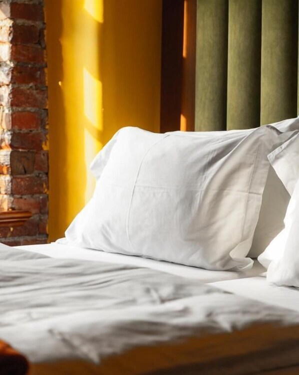 A neatly made bed with white linens in a room with a brick wall and a yellow accent wall.