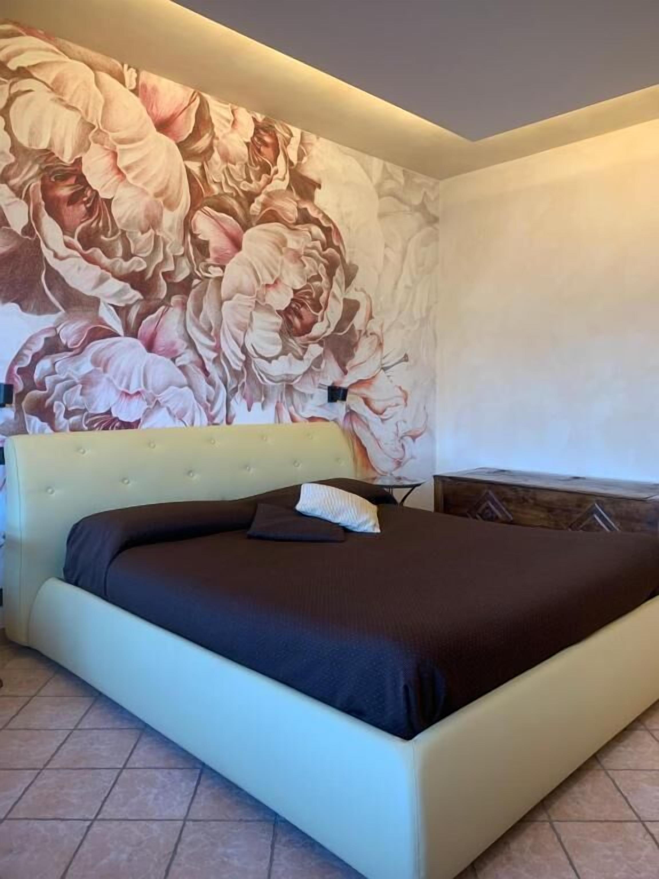 Quarto com um grande mural floral na parede, cabeceira estofada e cama com roupa de cama escura.