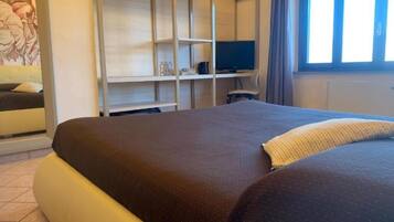 A bedroom with a large bed, a TV on a stand, and a wardrobe.
