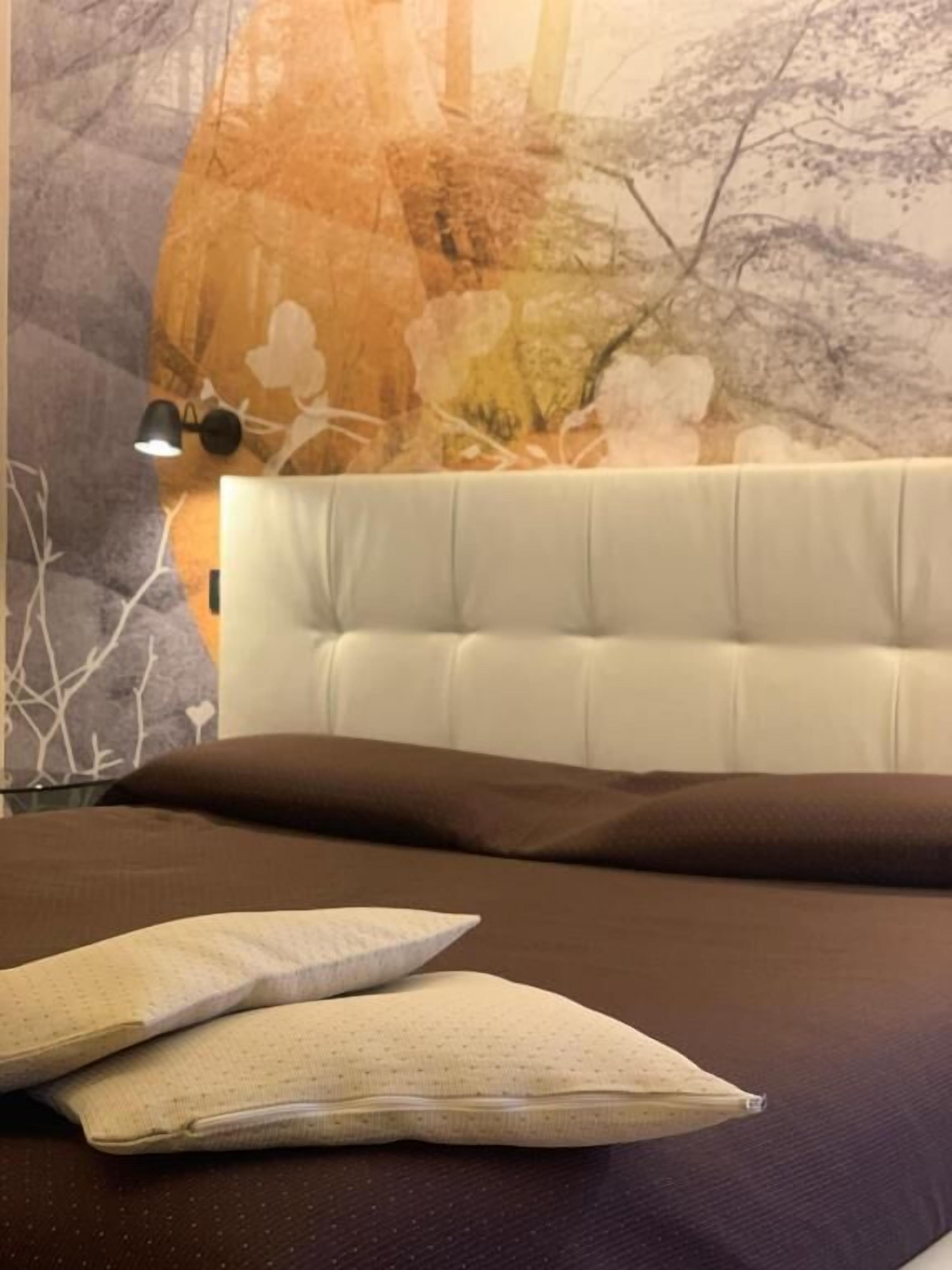 A bed with a white headboard, a brown pillow, and a white pillow with a grid pattern.