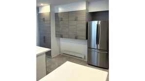 A modern kitchen with white cabinetry, a stainless steel refrigerator, and recessed ceiling lighting. - Luxury bungalow in Châteauguay (Châteauguay)