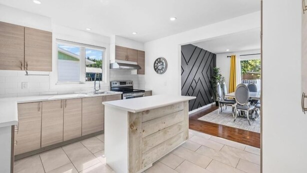 A modern kitchen with wooden cabinets, a white countertop, and a dining area with a table and chairs. - Luxury bungalow in Châteauguay (Châteauguay)